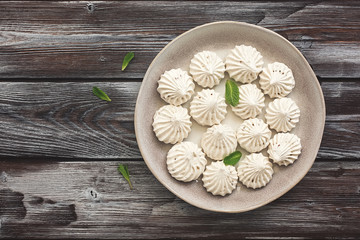 Tasty meringues in a plate on a dark wooden rustic background. Traditional french dessert. Top view, flat lay, copy space.