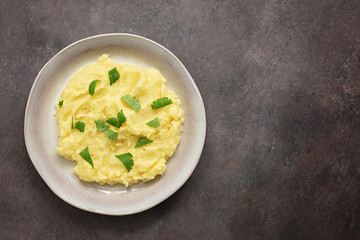 Mashed potatoes with greens in a plate on a dark background. Top view, flat lay, copy space.
