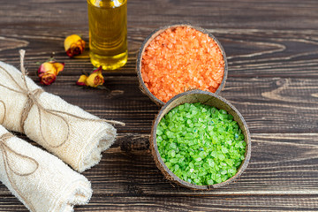 The concept of spa treatment, with natural, fragrant sea two-color bath salt and bath towels. In the background is oil from rose petals. On a wooden background.