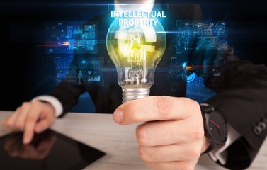 Businessman holding lightbulb with INTELLECTUAL PROPERTY inscription, online security idea concept