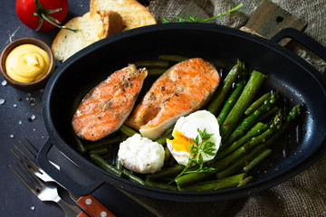 Green asparagus, grilled salmon and poached eggs. Healthy food on rustic wooden background.