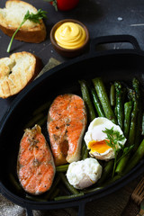 Green asparagus, grilled salmon and poached eggs. Healthy food on rustic wooden background.