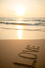Girl wrote the word love in the sand at sunset on the sea in thailand