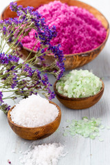 Sea salt in bowl, aroma oil in bottles, Wellness and flowers on grey textured background and flowers on vintage wooden background. Selective focus.