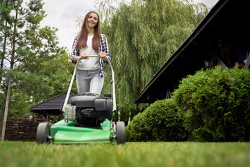Young female gardener using lawn mower.