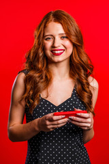 Girl with red hair using smartphone or surfing internet on studio background. Modern technology - apps, social networks