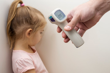 hand with an electronic thermometer is aimed at a small child. on the thermometer the temperature is 39.9