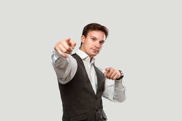 Young man in a white shirt and grey vest pointing his finger at the camera