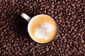 White coffee cup on a solid dark background of roasted coffee beans.