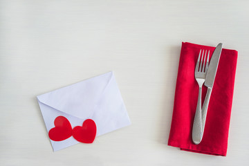 Romantic table setting. Beautiful cutlery on red napkin, two red hearts on white envelope