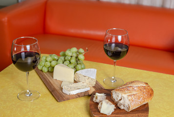 Red wine, cheese, bread and grapes on yellow table with orange background