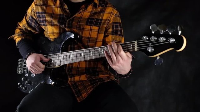 man plays electric bass guitar. Black background. the color of the guitar is black. average plan.