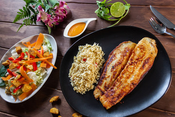 Pescado a la plancha con especias y ensalada de lechuga zanahoria y aderezo mil islas y limon arroz en mesa de madera