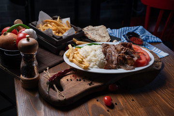 Turkish doner served in a plate with rice, patato and tomato, placed on a wooden table