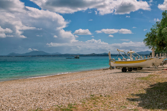 Beautiful idyllic summer landscape with beach, turquoise sea water, white boats for rent on the shore, blue sky with clouds and mountains on the horizon. Corfu Island, Barbati village, Greece