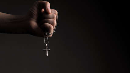 Close-up images of crucifix pendant necklace in man hand on black color background in studio which...