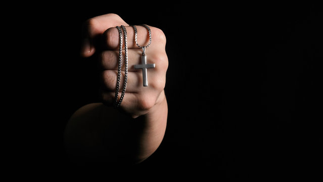 Close-up images of crucifix pendant necklace in man hand on black color background in studio which represent praying for god or jesus and thank gods for giving peaceful and faithful to people
