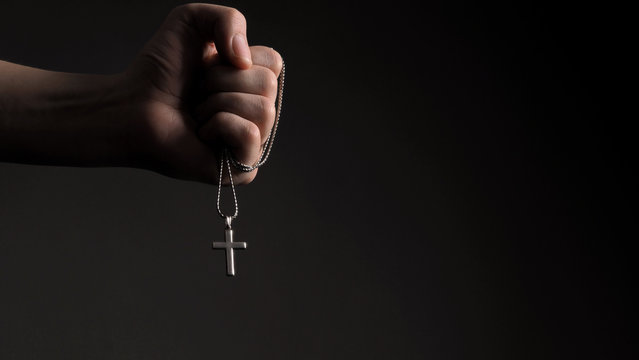 Close-up images of crucifix pendant necklace in man hand on black color background in studio which represent praying for god or jesus and thank gods for giving peaceful and faithful to people
