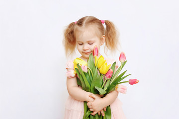 Little beautiful girl blonde with a bouquet of tulips on a light background. Baby girl smiling. Spring and women's day concept. Little girl holding a bouquet of colored tulips. Сopy spase