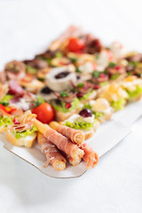 Bread sticks grissini with prosciutto and fresh beautiful decorated crostini on plate.