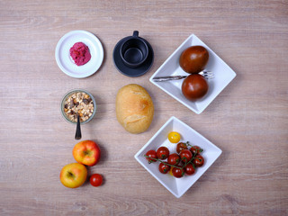 Fototapeta na wymiar Pretzel, sweet tea-cake, marmelade, avocado, tomatoes, a pomegranate and a glass of orange juice, symetrically arranged on a wooden table on white and black tableware