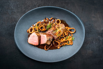 Traditioneller gebratener dry aged Rostbraten aufgeschnitten Röstzwiebel und würzige Bratensauce serviert als Draufsicht auf einem Modern Design Teller