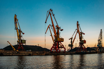 Fototapeta na wymiar Harbor cargo cranes on sunset sky background