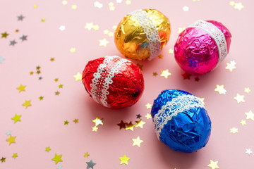 Easter composition. Colorful shiny easter eggs with stars confetti on pastel pink background. Flat lay, top view, copy space