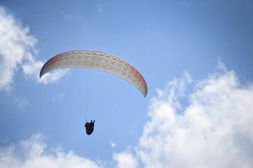 Paraglider flying on colored parachute in blue clear sky at a bright sunny summer day. Active lifestyle, extreme hobbies