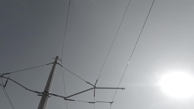 view of the poles and wires of electric vehicles against the cloudless sky with the bright sun