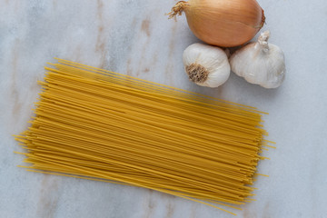 Uncooked spaghetti with raw garlic and onions on a countertop 