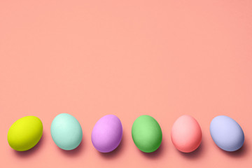 row of eggs of different colors on bottom on pink background with copyspace. happy easter