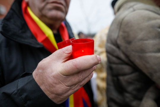 Shallow depth of field (selective focus) image with the hands of a man holding a candle outdoor on a rainy cold day.