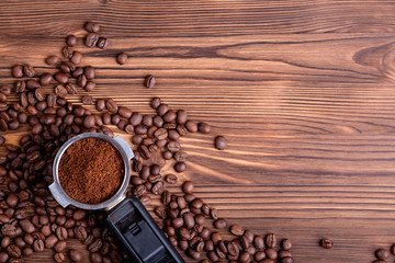 Roasted coffee beans and a porta filter with ground coffee on a brown wooden background with copyspace.