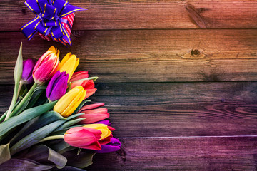 A bouquet of tulips and a small present on an iridescent wooden background