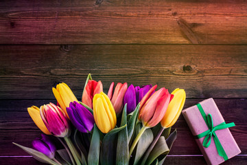 Multicolored tulips on a wooden background with a gift