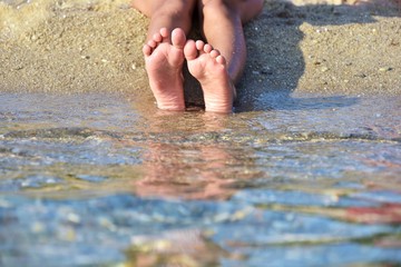 Girls bare feet at the transparent sea wave with golden sand, selective focus. Bare feet in a sea wave.  Relaxation in the ocean.  Woman feet in the water. Summertime. Barefoot girl plays with waves 