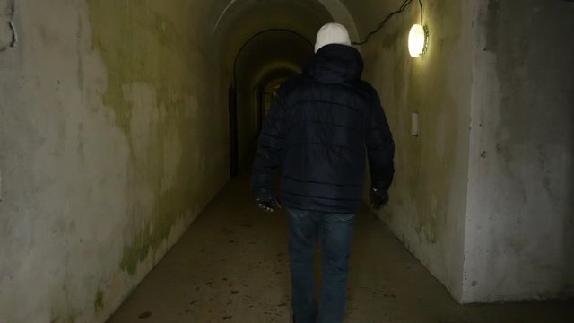 Man in a black jacket walks down a long dark tunnel