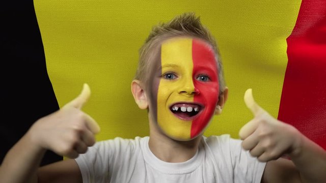 Joyful fan on the background of the flag of Belgium. Happy boy with painted face in national colors. The young fan rejoices in the victory of his beloved team. Success. Victory. Triumph.