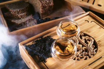 Chinese tea board with cups of hot green leaf tea Da Huan Pao and healthy cereal bread and prunes ready to serve. Close up menu tea ceremony for cafe or restaraunt