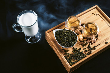 Obraz na płótnie Canvas Chinese tea ceremony with glass cups with milk Oolong tea on wooden board and black background. Traditional Asian drink, beautiful serving