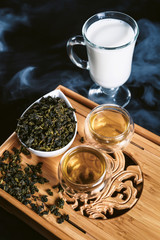 Chinese tea ceremony with glass cups with milk Oolong tea on wooden board and black background....