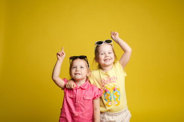Two happy beautiful stylish little girl wearing sunglasses posing isolated at yellow studio...