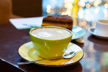 Close up and selected focus view on mug of coffee on brown wooden table. Hot coffee with latte art served with piece of orange-chocolate cake on turquoise dish plate. Cute kitten is on the coffee foam