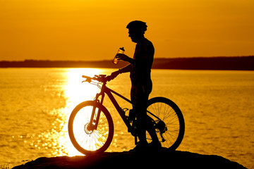 Fototapeta na wymiar silhouette of a cyclist with sunset background. Orange sky, hobby, healthy habbits. Drinking water while resting