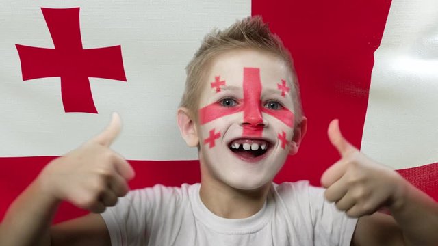 Joyful fan on the background of the flag of Georgia. Happy boy with painted face in national colors. The young fan rejoices in the victory of his beloved team. Success. Victory. Triumph.
