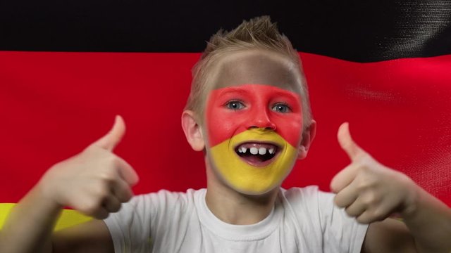 Joyful fan on the background of the flag of Germany. Happy boy with painted face in national colors. The young fan rejoices in the victory of his beloved team. Success. Victory. Triumph.