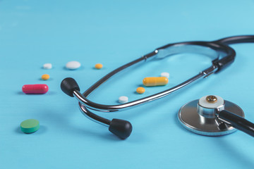 Stethoscope and multicolored tablets and capsules on a blue background