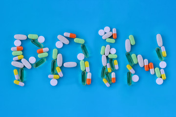 Written word "pain" made of a lot of multicoored pharmaceutical medicine tablets, pills and capsules. Metaphor and concept of medical supplements and health care.