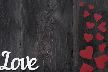 white lettering "Love" on a rustic background with red cardboard hearts on the side. with place for text